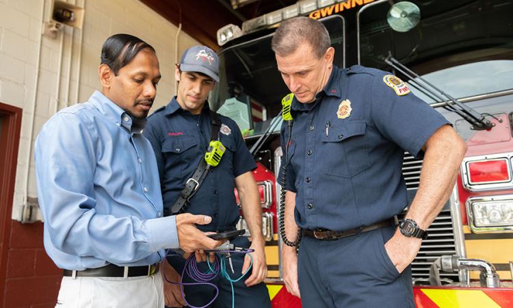 A researcher demonstrates technology to two firefighters
